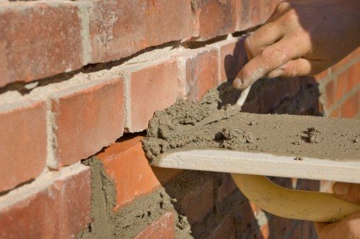 Worker placing mortar into the joints of an existing brick wall