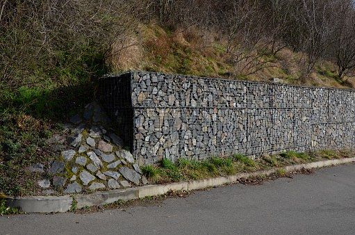 Stone-filled wire retaining structure supporting a slope beside a road