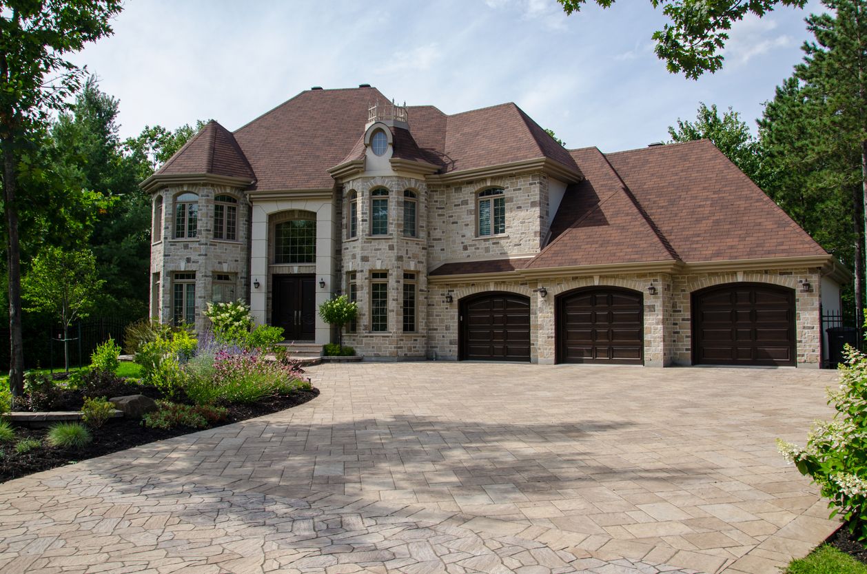 Three-car garage attached to a stone-faced home with a broad driveway approach