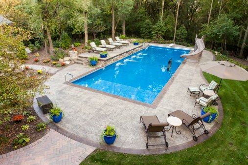 Concrete surround with lounge chairs and a dining area beside an outdoor swimming pool
