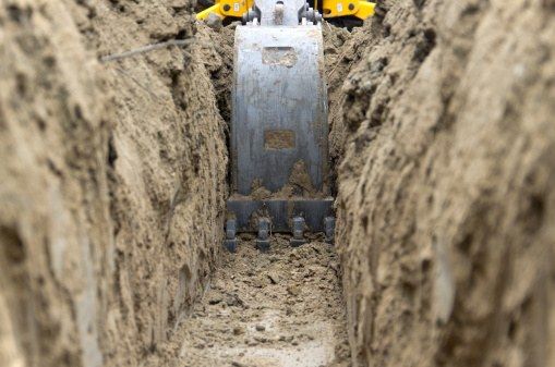 Excavator bucket digging a narrow trench through soil