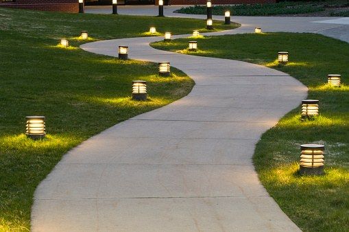 Curving concrete walkway through a lawn with small path lights